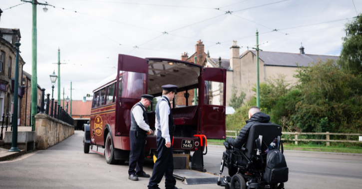 man in wheelchair is helped onto the accessible vehicle on the wheelchair lift by two people at Beamish Museum.